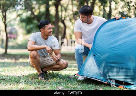 LGBTQIA Gay Paare campen zusammen im Wald für Urlaub und entspannen auf der Gitarre zusammen Stockfoto