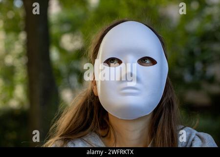 Frau mit weißer Vollgesichtsmaske, die im Wald sitzt Stockfoto