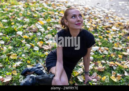 Frau sitzt auf Gras mit Herbstlaub Stockfoto