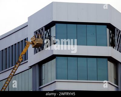 Kairo, Ägypten, 25. Januar 2024: Lackierservice und Instandhaltung des Außenbereichs eines Gebäudes, der Arbeiter befindet sich auf einem hydraulischen Löffelhubwagen, Stockfoto