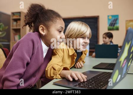 Seitliches Porträt zweier aufgeregter kleiner Kinder, die im Kopierraum der Schule auf den Computerbildschirm schauen Stockfoto