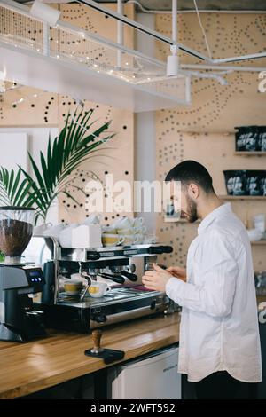 Ein Barista in der Nähe einer Espressomaschine bereitet leckeren Kaffee zu. Ein junger Mann bereitet Kaffee in einem Café zu. Stockfoto