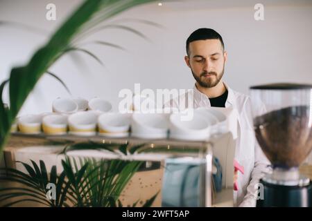 Ein Barista in der Nähe einer Espressomaschine bereitet leckeren Kaffee zu. Ein junger Mann bereitet Kaffee in einem Café zu. Stockfoto