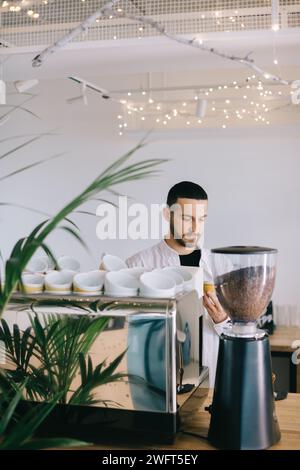 Ein Barista in der Nähe einer Espressomaschine bereitet leckeren Kaffee zu. Ein junger Mann bereitet Kaffee in einem Café zu. Stockfoto