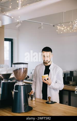 Ein Barista in der Nähe einer Espressomaschine bereitet leckeren Kaffee zu. Ein junger Mann bereitet Kaffee in einem Café zu. Stockfoto