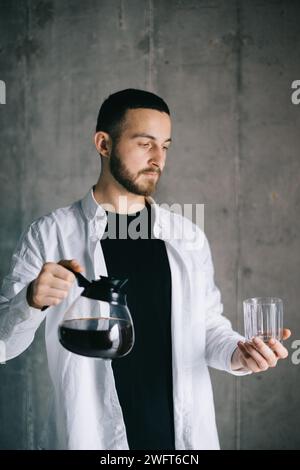 Ein schöner Barista, der frisch gebrühten Tropfkaffee in eine Tasse aus Glas gießt. Zubereitung von Kaffee – Alternative Methode. Stockfoto