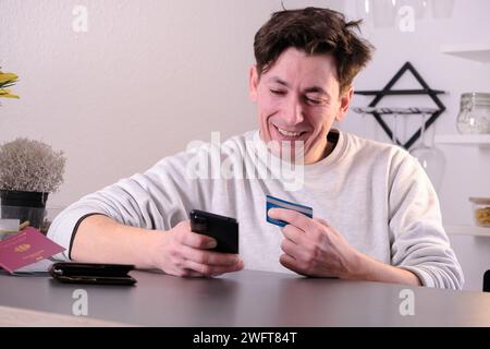 Ein glücklicher Mann am Telefon mit einer Kreditkarte in der Hand, Reisepass und Brieftasche auf dem Tisch Stockfoto