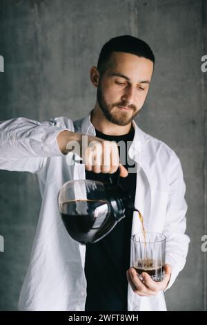 Ein schöner Barista, der frisch gebrühten Tropfkaffee in eine Tasse aus Glas gießt. Zubereitung von Kaffee – Alternative Methode. Stockfoto