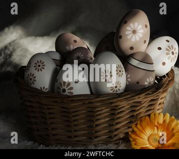 Gemalte ostereier in einem Korb auf einem weichen weißen Hintergrund mit Ringelblumen Stockfoto