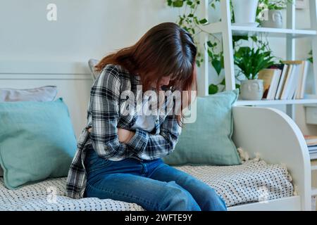 Junge Frau mit Magenschmerzen, die zu Hause auf der Couch sitzt Stockfoto