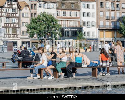 Straßburg, Frankreich - 2. Juli 2023: Gruppe junger Menschen Mädchen Frauen, die an einem warmen, sonnigen Tag auf Bänken am Brunnen der Stadt sitzen. Place Kleber Straßburg Stockfoto