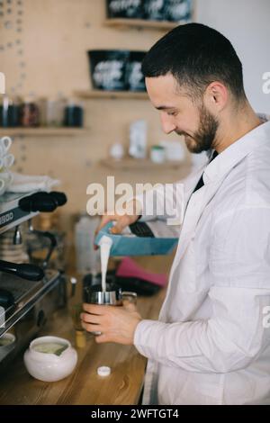 Ein Barista gießt Milch aus einem Karton. Der Prozess der Zubereitung von Kaffee oder Matcha. Stockfoto