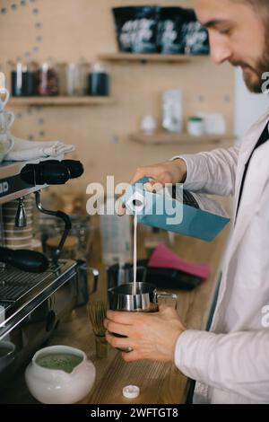 Ein Barista gießt Milch aus einem Karton. Der Prozess der Zubereitung von Kaffee oder Matcha. Stockfoto