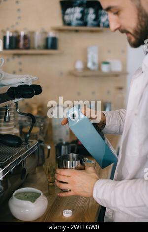 Ein Barista gießt Milch aus einem Karton. Der Prozess der Zubereitung von Kaffee oder Matcha. Stockfoto