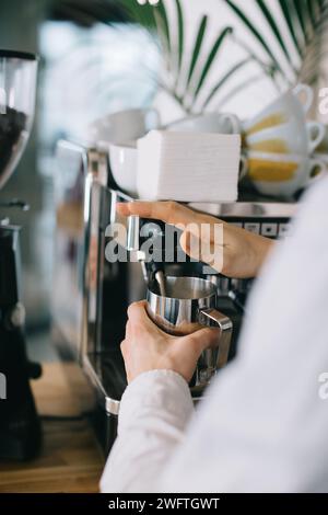 Ein Barista bereitet mit einer Espressomaschine Milch für Cappuccino zu. Nahaufnahme eines Mannes, der Kaffee in einem Café zubereitet. Stockfoto