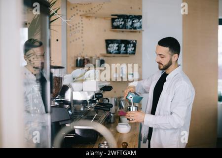 Ein Barista in der Nähe einer Espressomaschine bereitet leckeren Kaffee zu. Ein junger Mann bereitet Kaffee in einem Café zu. Stockfoto