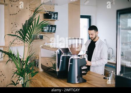 Ein Barista in der Nähe einer Espressomaschine bereitet leckeren Kaffee zu. Ein junger Mann bereitet Kaffee in einem Café zu. Stockfoto