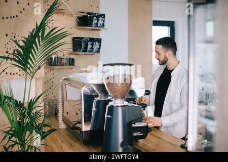 Ein Barista in der Nähe einer Espressomaschine bereitet leckeren Kaffee zu. Ein junger Mann bereitet Kaffee in einem Café zu. Stockfoto
