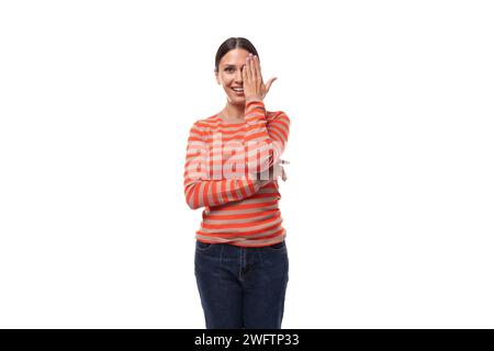 Eine 30-jährige, schlanke europäische Frau in einer lässigen orangefarbenen Bluse flirtet, während sie ihr Gesicht mit der Hand bedeckt Stockfoto