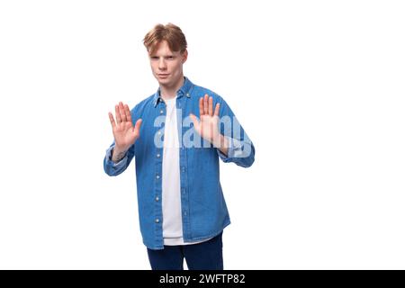 Der junge, gut gepflegte kaukasische rothaarige Mann in einem Jeanshemd gestikuliert aktiv Stockfoto