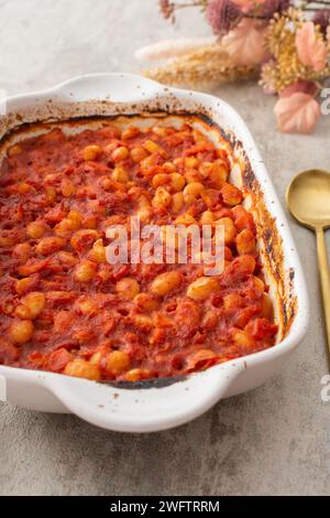 Gesundes Frühstück und Mittagessen, gedünstete weiße Bohnen mit Karotten, Zwiebeln und Tomaten, Blick von oben auf eine ovale Keramikrösterei mit gedünsteten Hülsenfrüchten Stockfoto