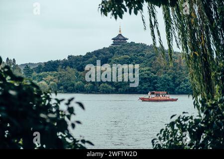 Ein kleines Boot schwimmt sanft zwischen üppigen Bäumen, umgeben von ruhigen Gewässern: Dem Westsee von Hangzhou Stockfoto