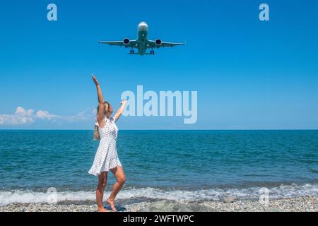 Seaside Escapade: Mädchen in weißem Kleid auf Steinen, Flugzeug umarmt das Blaue Meer Stockfoto