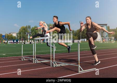 Zwei AthletInnen, Frau und Mann, die im Freien im Stadion Hürden laufen Stockfoto