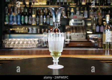 Klassische Art der Absinthpräparation mit Brouiller (ein Werkzeug zur Herstellung von Absinth). Glas mit Absinth auf Bartheke in Nahaufnahme. Stockfoto