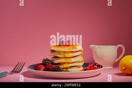 Stapel Pfannkuchen mit gemischten Beeren und garniert mit Honig auf rosa Hintergrund. Stockfoto