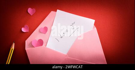 Love Note mit Nachricht Ich liebe dich in einem rosa Umschlag auf rotem Hintergrund mit rotem Farbverlauf mit rosa Herzen und Bleistift. Draufsicht. Stockfoto