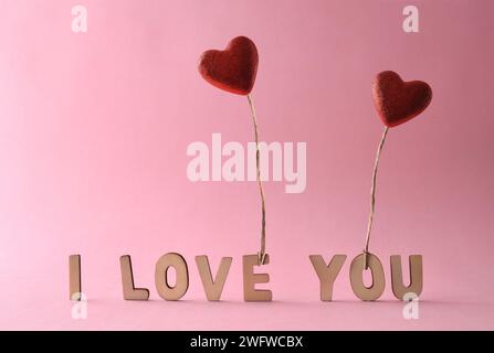 Liebe Hintergründe mit Ausschnitten aus Buchstaben, die den Satz i Love You bilden, und zwei roten Herzballons mit Glitzer, die von einem fliegenden Jutefaden gehalten werden. Vorn VI Stockfoto