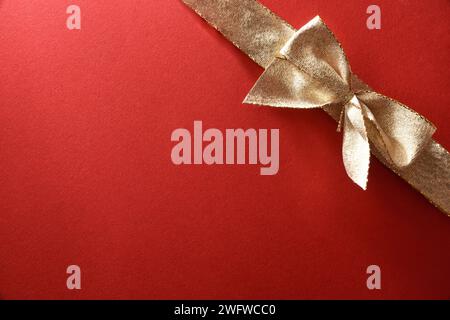 Hintergrunddetail aus Geschenkverpackung mit goldener Schleife in einer Ecke auf strukturiertem rotem Papier. Draufsicht. Stockfoto