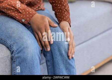 Ein Nahaufnahme eines Körperteils. Die Hände der afroamerikanischen jungen Frau halten ihr Bein, sie spürt starke Schmerzen im Knie. Stockfoto