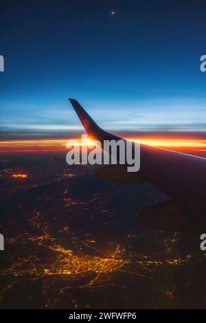 Flugzeugflug bei Sonnenuntergang über der Erde des Lichts der Stadt und Flügel des Flugzeugs. Blick vom Fenster des Flugzeugs. Reisen in der Luft. Stockfoto