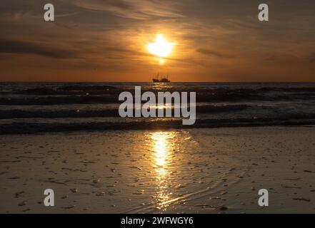 Fischerboot an der Küste direkt unter der Sonne bei Sonnenuntergang. Am Ende des Tages fährt ein Fischerboot auf dem Weg vorbei, um Fische zu fangen. Stockfoto