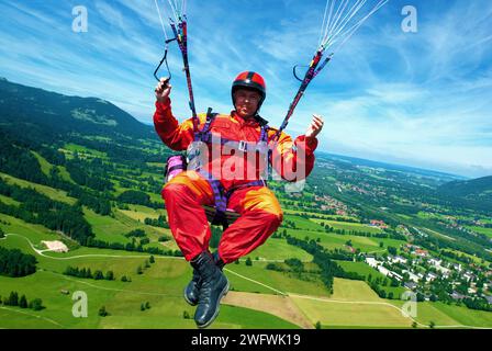 Ein Gleitschirmflieger in Orange und Rot fliegt über die Wiesen bei Brauneck bei Lenggries, Bayern, Deutschland, Europa Stockfoto