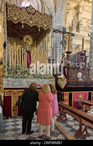 Jerez de la Frontera, Spanien - 01. Februar 2024: Drei Frauen sehen einen Kirchenaltar mit goldenen Details, Blumen und religiösen Ikonen in Jerez de Stockfoto