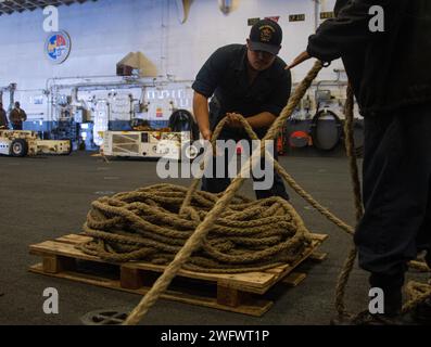 PHILIPPINE SEA (20. Januar 2024) Seaman Antonio Ruiz aus San Diego, der dem vorgelagerten amphibischen Angriffsträger USS America (LHA 6) zugeteilt wurde, wickelt während einer Replenishment-at-Sea mit dem Flottennachfüllöler USNS John Ericsson (T-AO-194) eine Linie in der Hangarbucht des Schiffes, am 20. Januar, auf See. America, Leitschiff der America Amphibious Ready Group, ist im Einsatzgebiet der 7. US-Flotte im Einsatz. Die 7. US-Flotte ist die größte nach vorne gerichtete nummerierte Flotte der US Navy und interagiert routinemäßig mit Verbündeten und Partnern, um eine freie Flotte zu erhalten Stockfoto