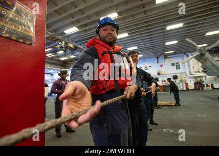 PHILIPPINISCHE SEE (20. Januar 2024) Seaman Demetrius Pierce aus Detroit, der dem vorwärtsgerichteten amphibischen Angriffsträger USS America (LHA 6) zugeteilt wurde, bewegt sich auf einer Linie in der Hangarbucht des Schiffes während einer Auffüllung auf See mit dem Flottenauffüllöler USNS John Ericsson (T-AO-194), während er in der Philippinischen See segelt, Jan. 20. America, Leitschiff der America Amphibious Ready Group, ist im Einsatzgebiet der 7. US-Flotte im Einsatz. Die U.S. 7th Fleet ist die größte nach vorne gerichtete nummerierte Flotte der US Navy und interagiert routinemäßig mit Verbündeten und Partnern im Preser Stockfoto