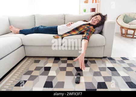 Foto des faulen Funky Guy trägt kariertes Hemd liegend Couch, der versucht, den fernseher fernzuhalten im Haus des Zimmers Stockfoto