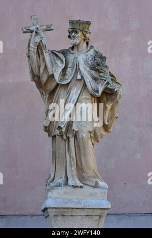 Steinstatue des heiligen in langem Gewand mit Kruzifix in der rechten Hand. Standort: Hainburg an der Donau Österreich Stockfoto