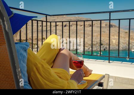 Frau mit einem Glas Wein entspannt sich auf einem Balkon mit Blick auf das Meer. Stockfoto