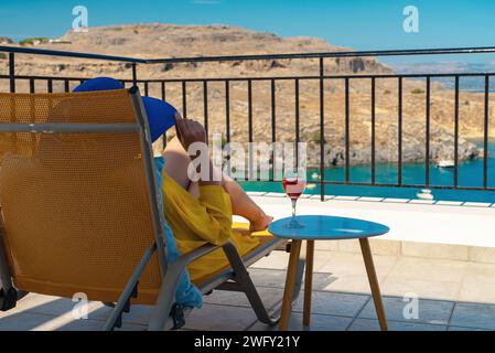 Frau mit einem Glas Wein entspannt sich auf einem Balkon mit Blick auf das Meer. Stockfoto