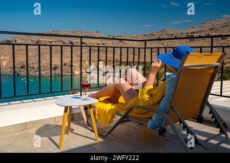 Frau mit einem Glas Wein entspannt sich auf einem Balkon mit Blick auf das Meer. Stockfoto