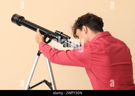 Junger Mann, der Sterne durch ein Teleskop auf beigefarbenem Hintergrund betrachtet Stockfoto