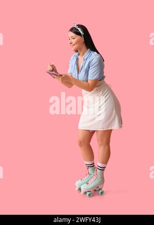 Schöne junge Kellnerin mit Notizbuch auf Rollschuhen vor rosa Hintergrund Stockfoto