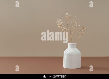 Weiße Vase mit trockenen Blumen auf braunem Tisch und beigefarbenem Hintergrund. Stilvoller und minimalistischer Hintergrund für Ihre Produkte und Texte. Skandina Stockfoto