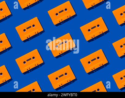 Muster mit orangen Retro-Audiokassetten auf blauem Hintergrund. Kreatives Konzept der Retro-Technologie. Ästhetik der 80er Jahre. Vintage-Audio Stockfoto