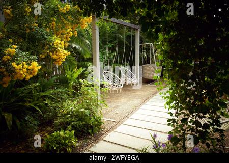 Weißer Boho-Schaukelstuhl im Freien mit niemandem in einem wunderschönen, entspannenden und gemütlichen Garten Stockfoto
